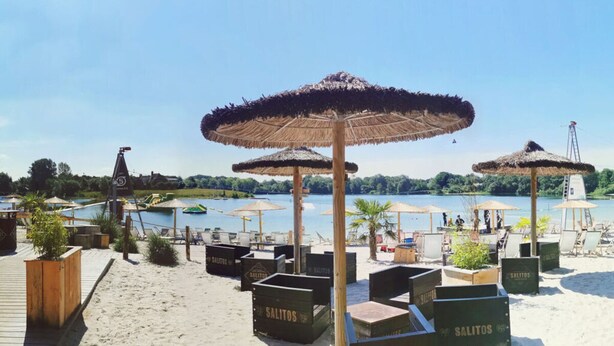 Een strandgebied met rieten parasols, ligbedden en houten kratten met de tekst 'SALITOS'.