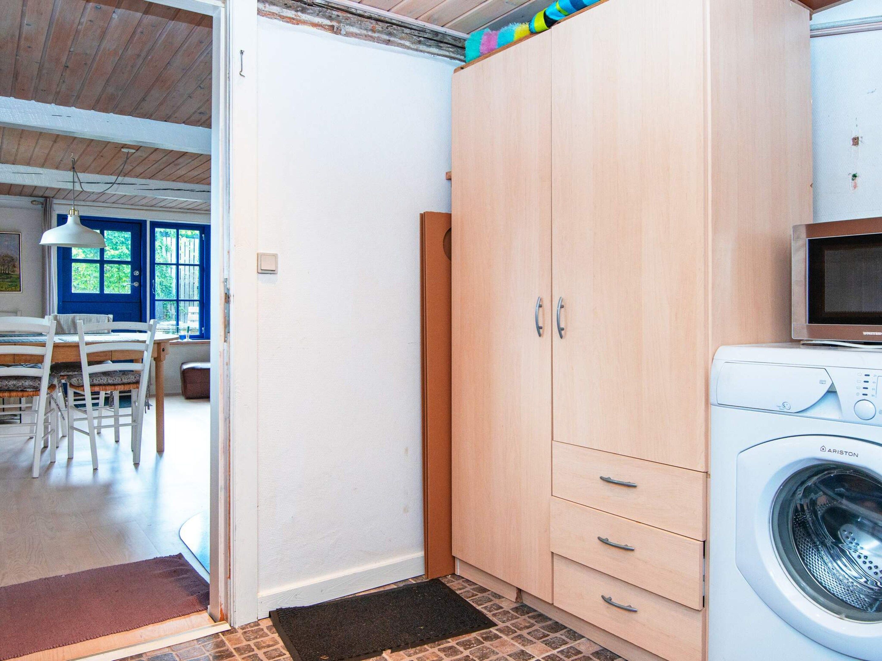 A laundry room with a washing machine, a microwave, and a wooden wardrobe.