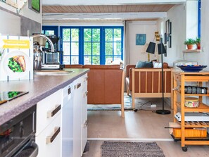 A compact kitchen with a coffee maker, a dining area with a wooden table and chairs, and a view through a blue-framed window. - 6 Person Holiday Home in Orsted (Ørsted)