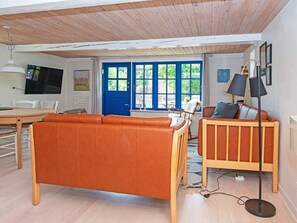 A living room with a sofa, a chair, a TV, and a window with a blue door. - 6 Person Holiday Home in Orsted (Ørsted)