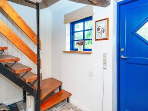 Een trap met houten treden en zwarte leuningen, een blauwe deur, een raam met uitzicht op groen, en een ingelijst schilderij aan de muur.