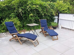Two wooden lounge chairs with blue cushions and a small wooden table, set on a patio with a hedge in the background. - 6 Person Holiday Home in Orsted (Ørsted)