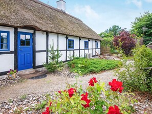 A traditional thatched-roof cottage with a blue door and windows, surrounded by a gravel garden with red flowers. - 6 Person Holiday Home in Orsted (Ørsted)