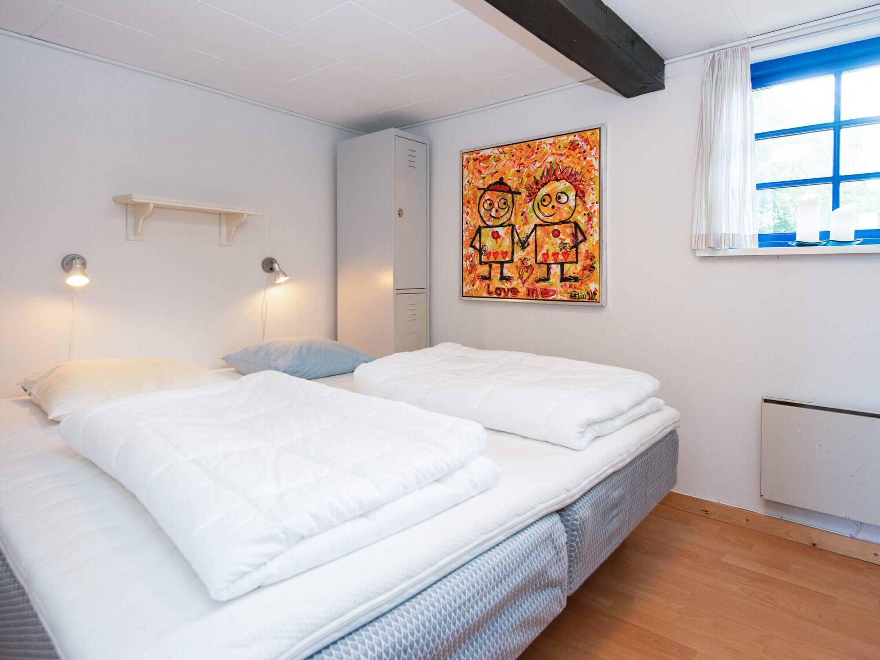 A bedroom with two beds, a radiator, a window with blue trim, and a wall-mounted artwork.