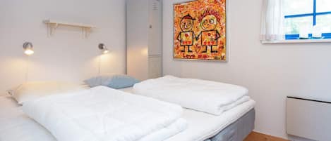A bedroom with two beds, a radiator, a window with blue trim, and a wall-mounted artwork.