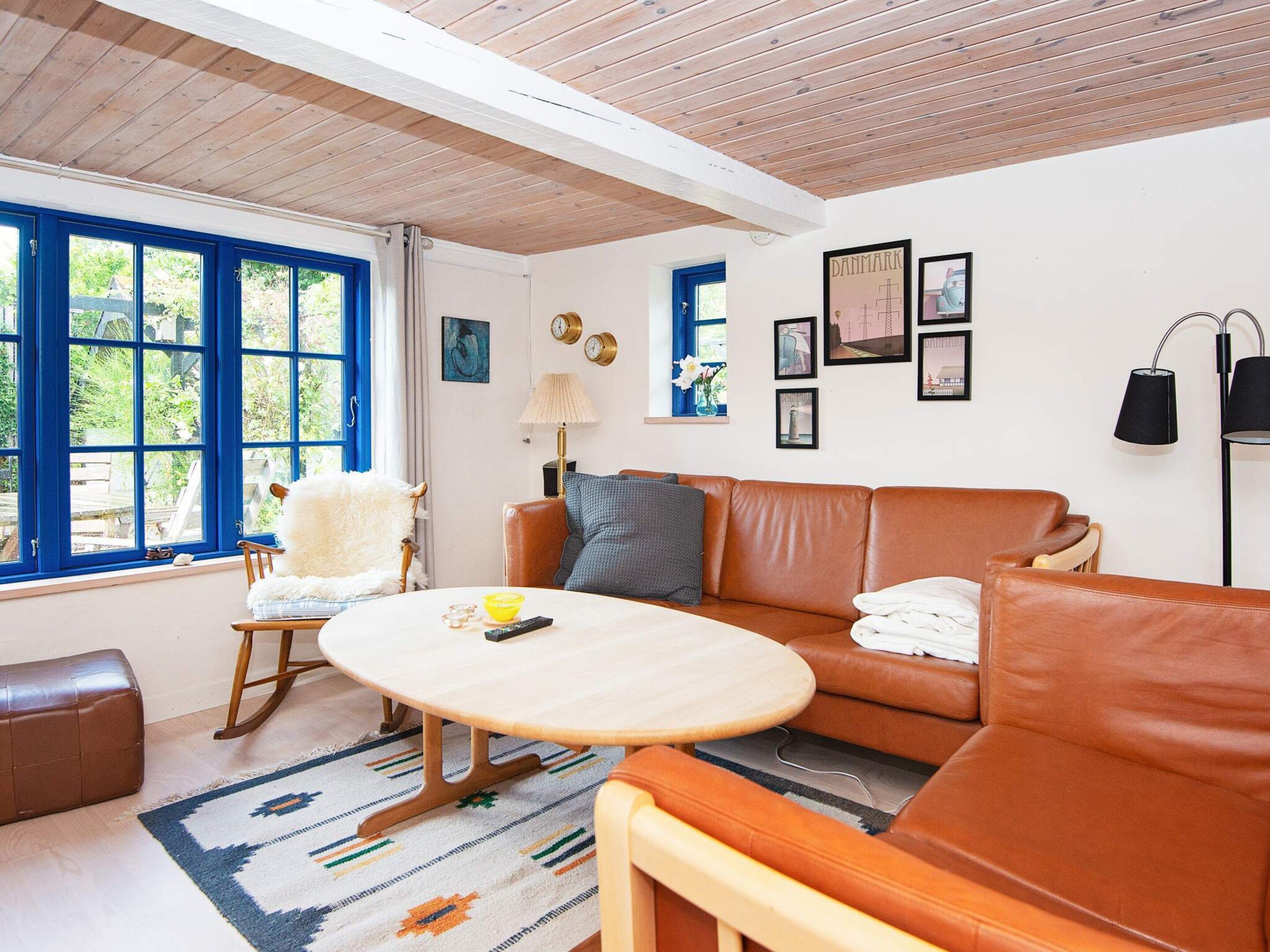 A room with a brown leather sofa, a wooden rocking chair, a round wooden table, and a patterned rug.