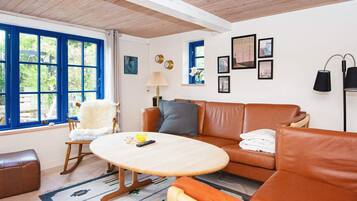 A room with a brown leather sofa, a wooden rocking chair, a round wooden table, and a patterned rug.