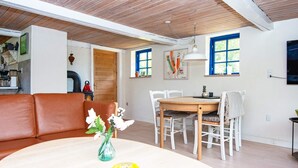 A modern living room with a brown leather sofa, a wooden dining table with chairs, and a vase with flowers. - 6 Person Holiday Home in Orsted (Ørsted)