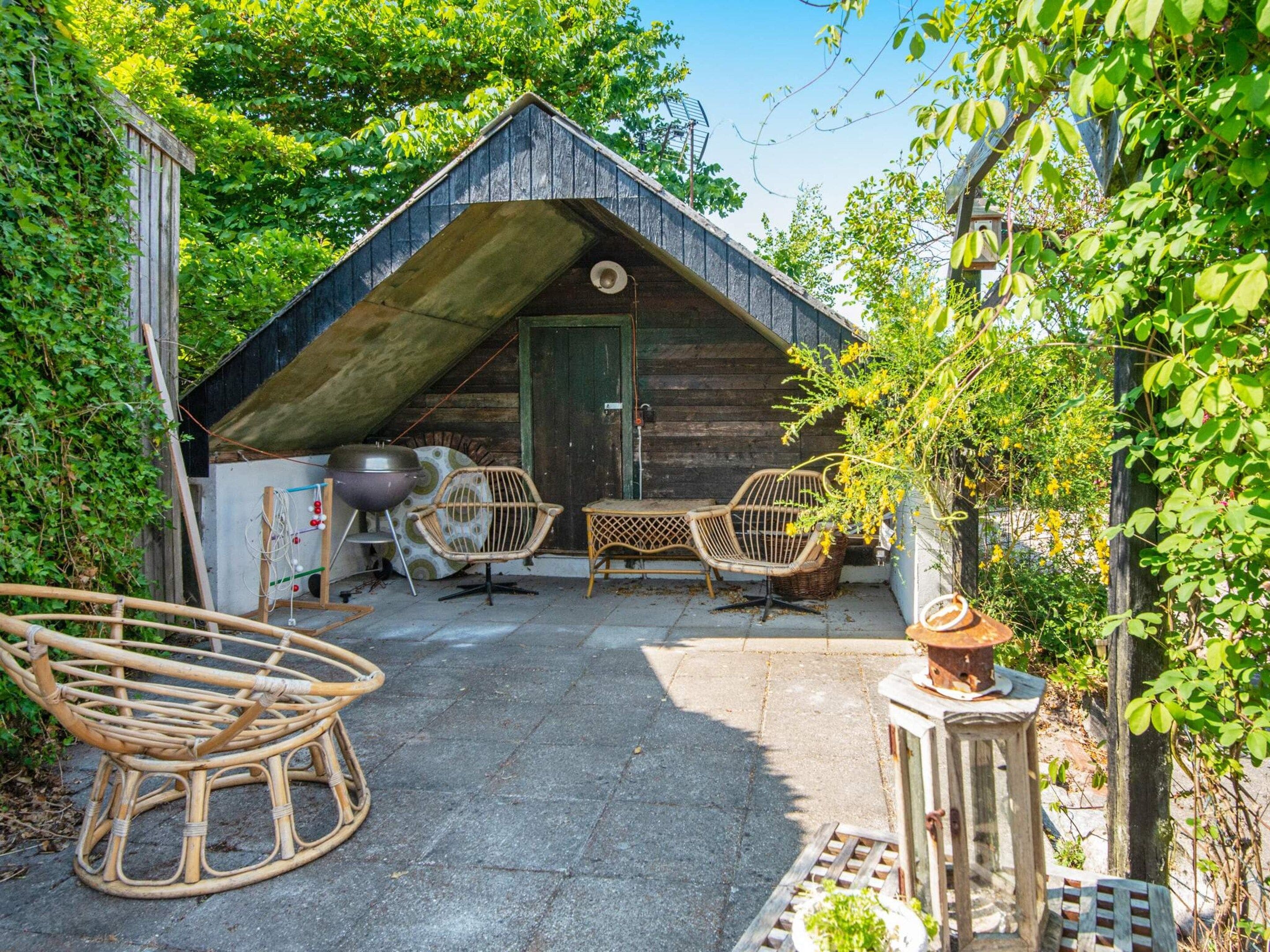 A wooden cabin with a sloped roof, two wicker chairs, a small table, and a lantern.