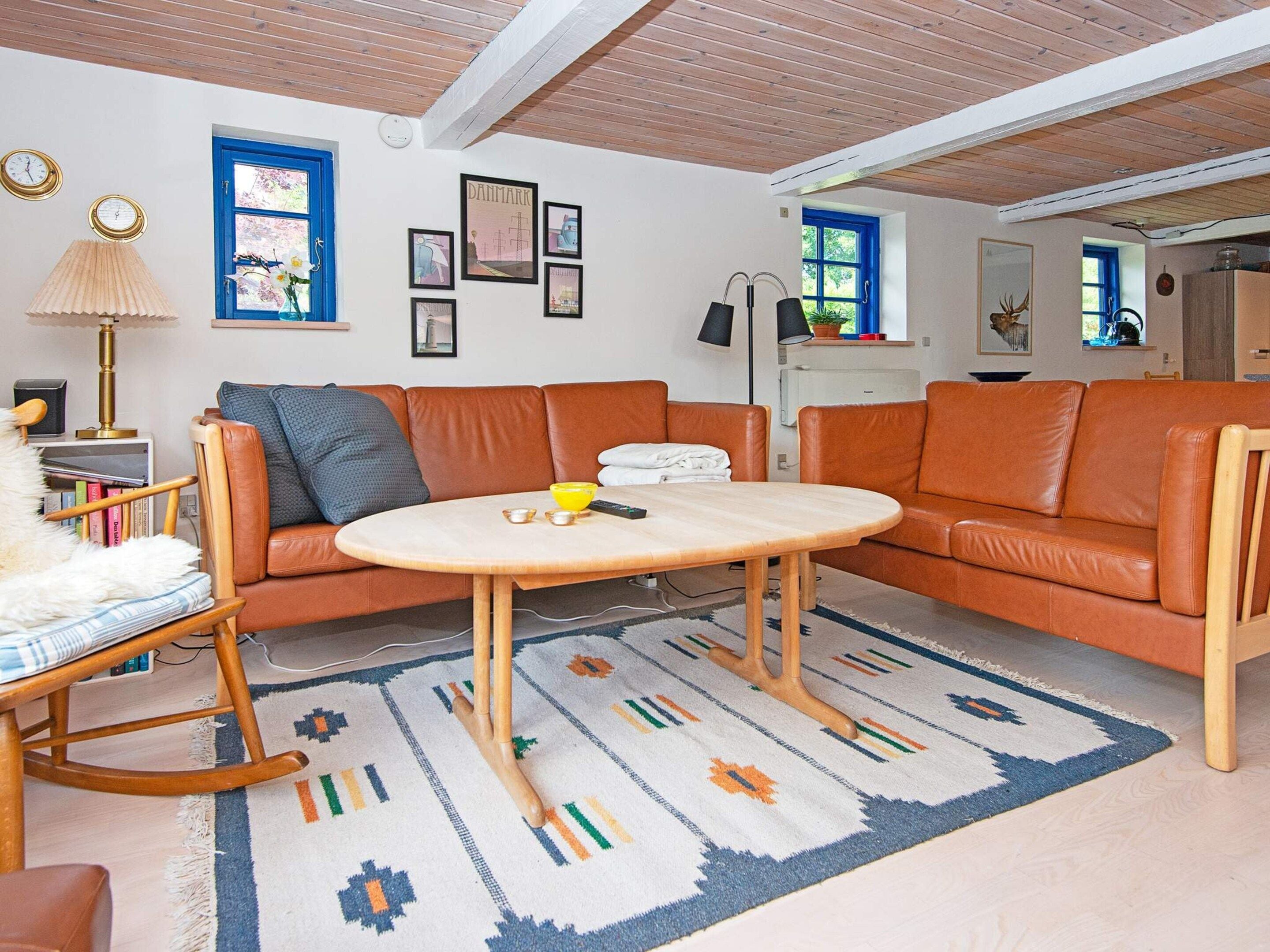 Een woonkamer met een bruine leren bank, een ronde houten tafel en een kamerkleed met dessin.