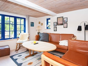 A room with a brown leather sofa, a wooden rocking chair, a round wooden table, and a patterned rug. - 6 Person Holiday Home in Orsted (Ørsted)