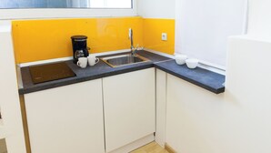 Een kleine keuken met een zwart aanrecht, witte kastjes, een koffiezetapparaat en een spoelbak.