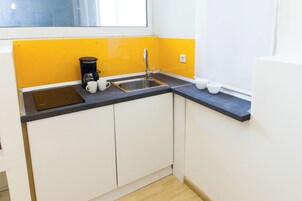 Una cocina pequeña con encimera negra, armarios blancos, cafetera y pileta.