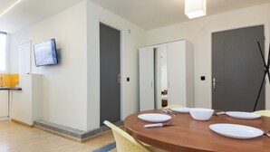 Een moderne eetruimte met een ronde houten tafel, gele stoelen en een flatscreen televisie aan de muur.