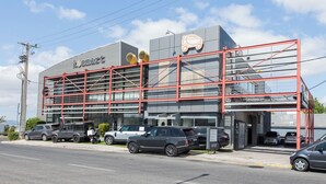 Een modern gebouw met een opvallend 'KOSMART' bord, met een auto-icoon en een rode metalen constructie.