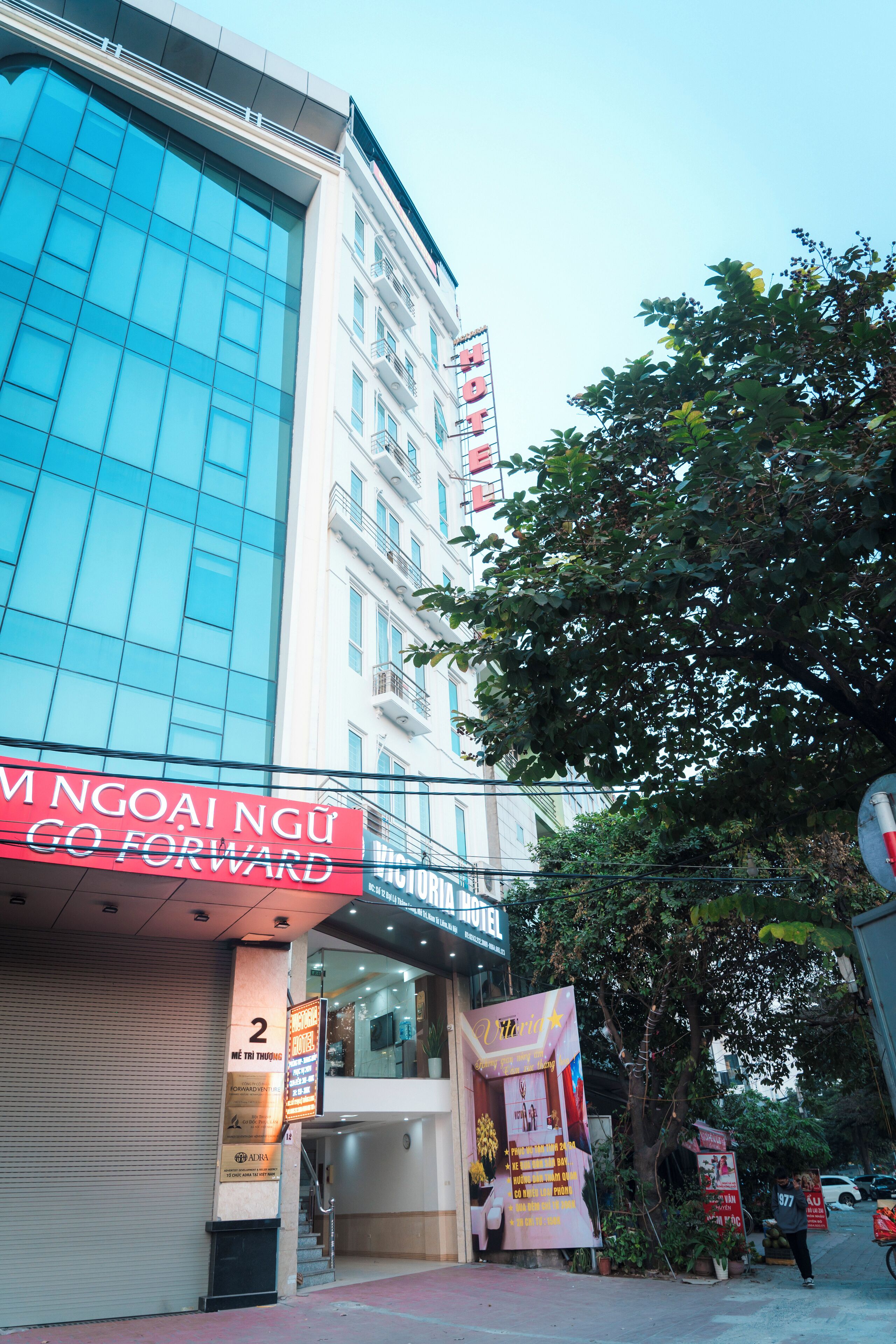 Un edificio de hotel con una amplia fachada de vidrio, un letrero que dice "Hotel" y un estandarte rojo con "MNGOAI NGU GO FORWARD".