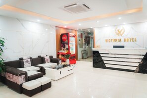 A modern hotel lobby with a reception desk, seating area, and a Coca-Cola refrigerator. - Victoria Hotel Me Tri (Hanoi)