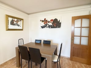 Un coin repas avec une table en bois et quatre chaises, un tableau encadré au mur et une porte dont les panneaux sont en verre dépoli.