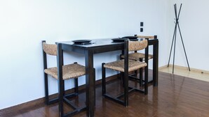 Un comedor con una mesa y sillas de madera oscura, una lámpara de pie negra y una pared blanca.