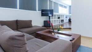 Una sala de estar moderna con un televisor de pantalla plana grande, un sofá marrón y una mesa de centro de madera con un jarrón de flores.
