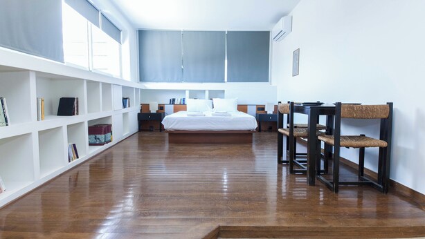 Un dormitorio amplio con una cama grande, piso de madera, estanterías blancas y una zona de comedor con mesa y sillas.