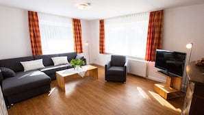 A modern living room with a sofa, armchair, coffee table, and TV. - Pleasant Apartment in Suddorf (Nebel)