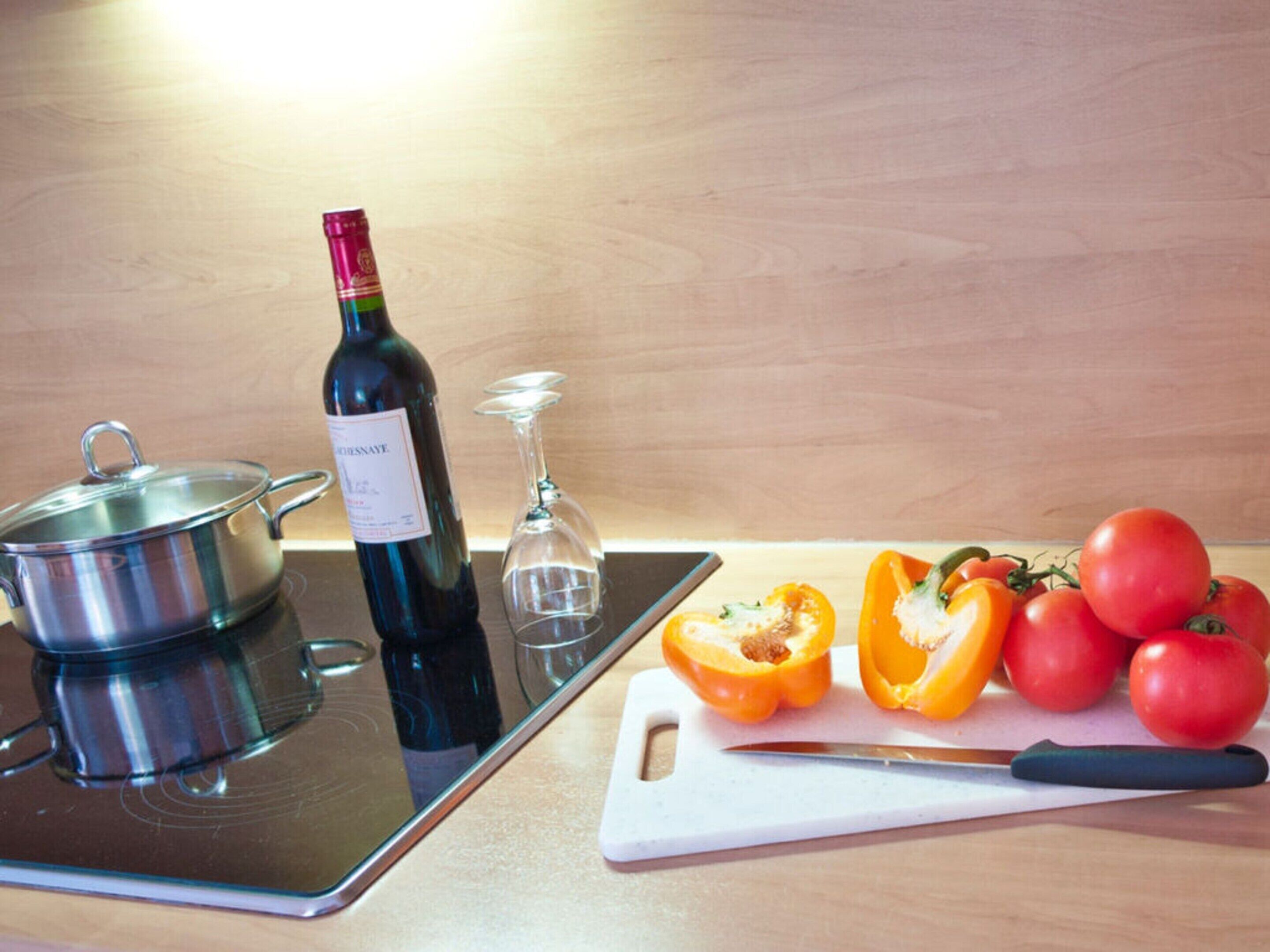 A kitchen with a stove, a wine bottle, a glass, and some vegetables on a cutting board.