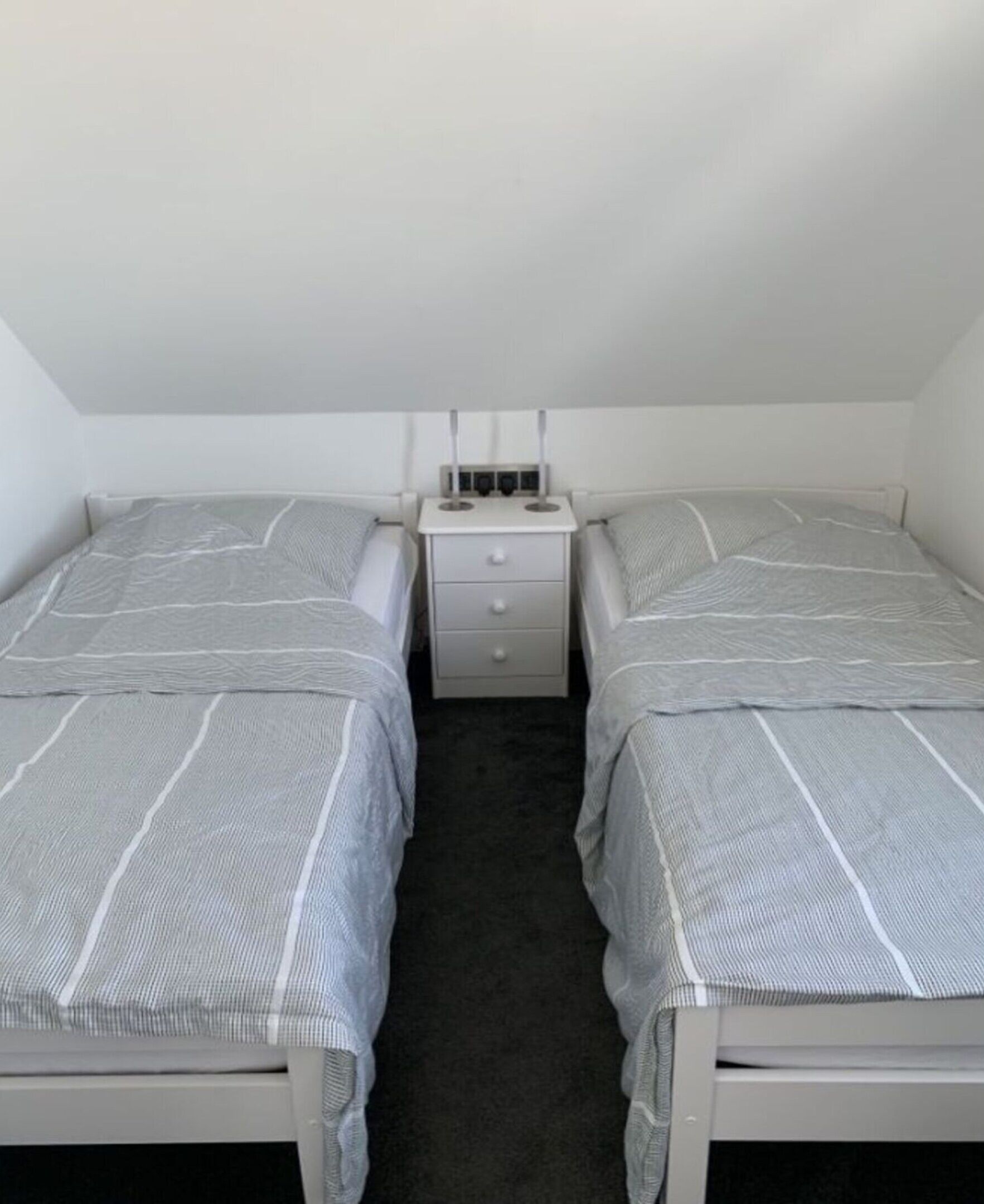 A small, single-room bedroom with two twin beds, a nightstand, and a dresser.
