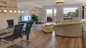 A modern living room with a glass dining table, black chairs, a beige sofa, and a TV. - Holiday Apartment Schliekieker (Kappeln)