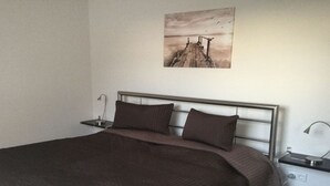 A bedroom with a bed, two bedside tables, and a wall-mounted picture. - Holiday Apartment Schliekieker (Kappeln)