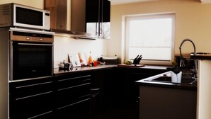 A compact kitchen with a microwave, oven, and stove, wooden cabinets, a window, and a sink. - Holiday Apartment Schliekieker (Kappeln)