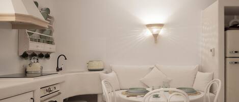 A compact kitchen with white appliances, a dining area with a round table and chairs, and a wall-mounted light fixture.