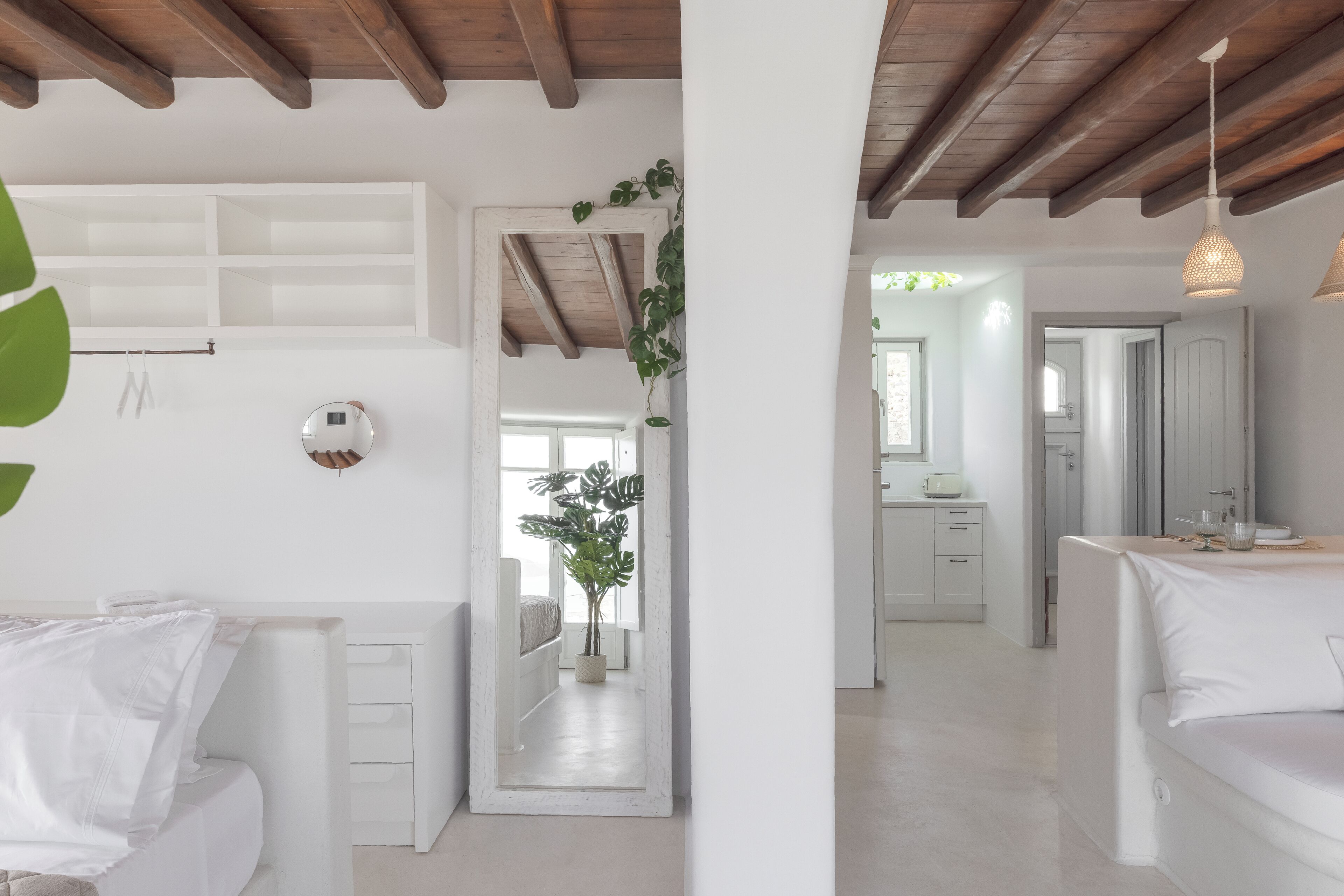 A modern, minimalist room with white furniture, a wooden ceiling, and a large mirror.