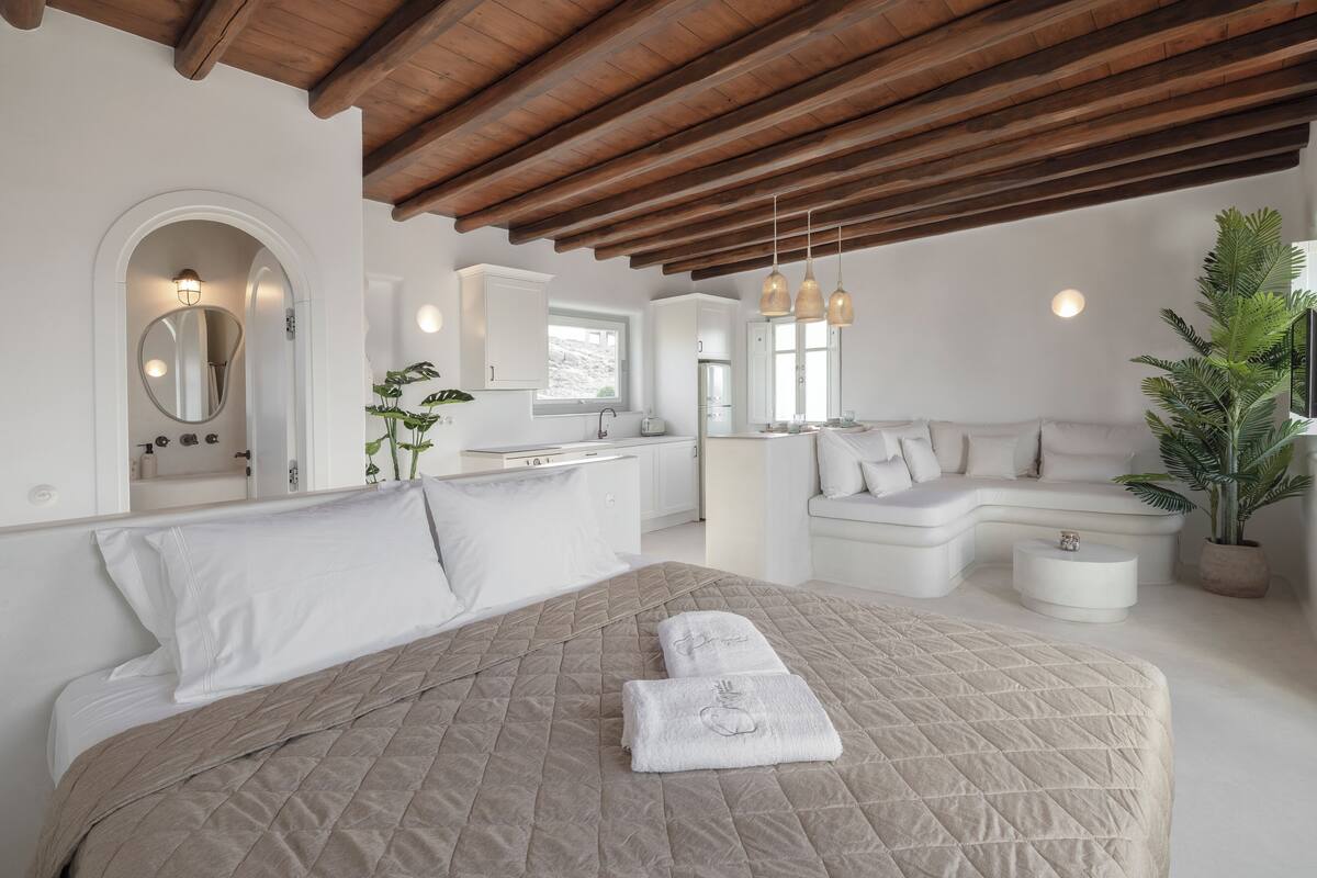 A modern bedroom with a large bed, a sofa, and a kitchen area.