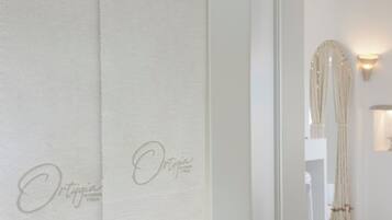 A hotel room with a white curtain featuring the name "Ortigia" and a wall-mounted light fixture.