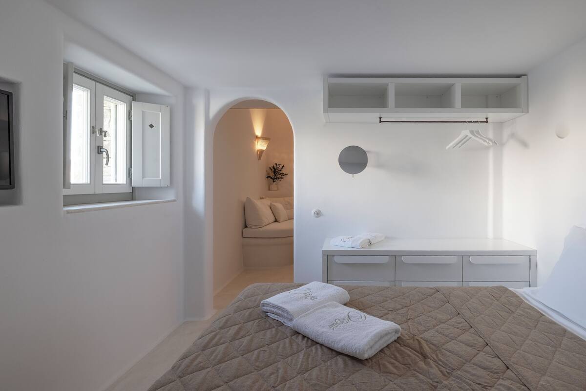A bedroom with a bed, a bedside table, a wardrobe, a window, and a door leading to a bathroom.