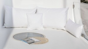 Un dormitorio moderno con diseño blanco, con un ventanal circular, una cama con ropa de cama blanca y una mesita de vidrio redonda con una revista.