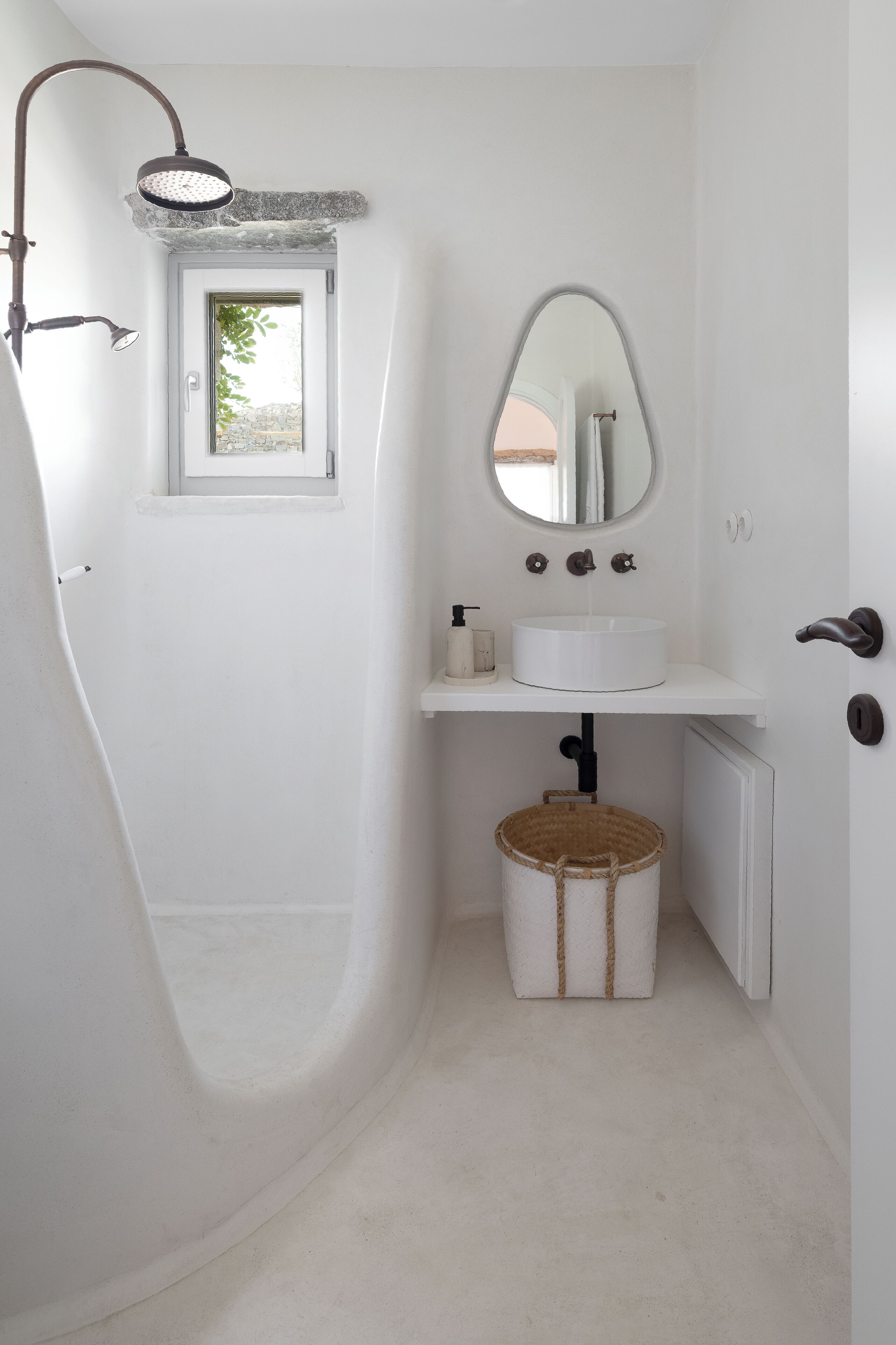 A bathroom with a white sink, a mirror, a shower, and a small window.