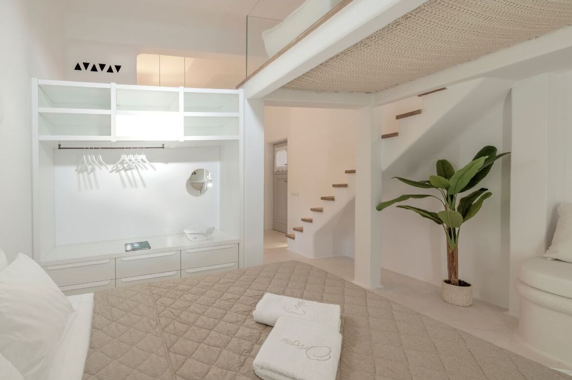 Une chambre d’hôtel moderne avec un lit, une armoire blanche, une plante et un escalier.