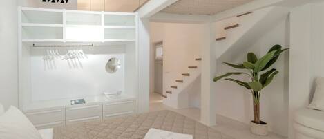 Une chambre d’hôtel moderne avec un lit, une armoire blanche, une plante et un escalier.