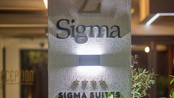 A sign for Sigma Suites Hotel with a reception area in the background.