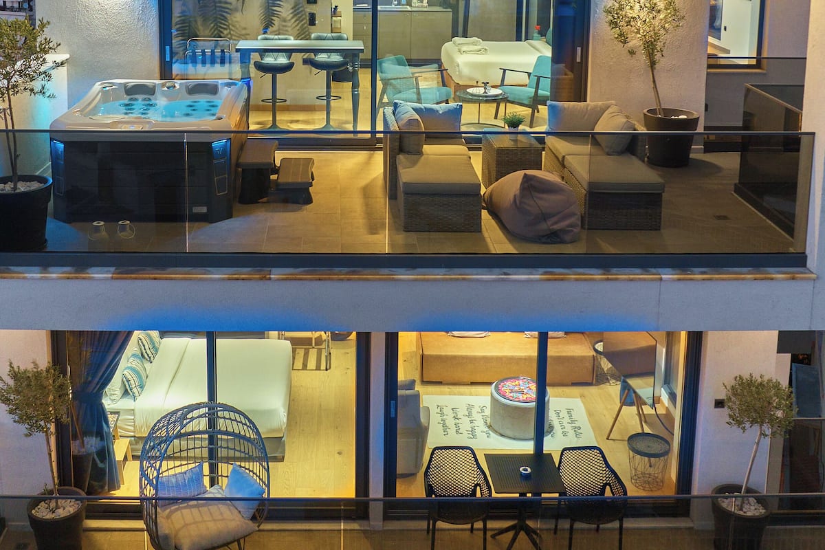 A modern two-story building with a rooftop terrace, glass walls, and a hot tub.