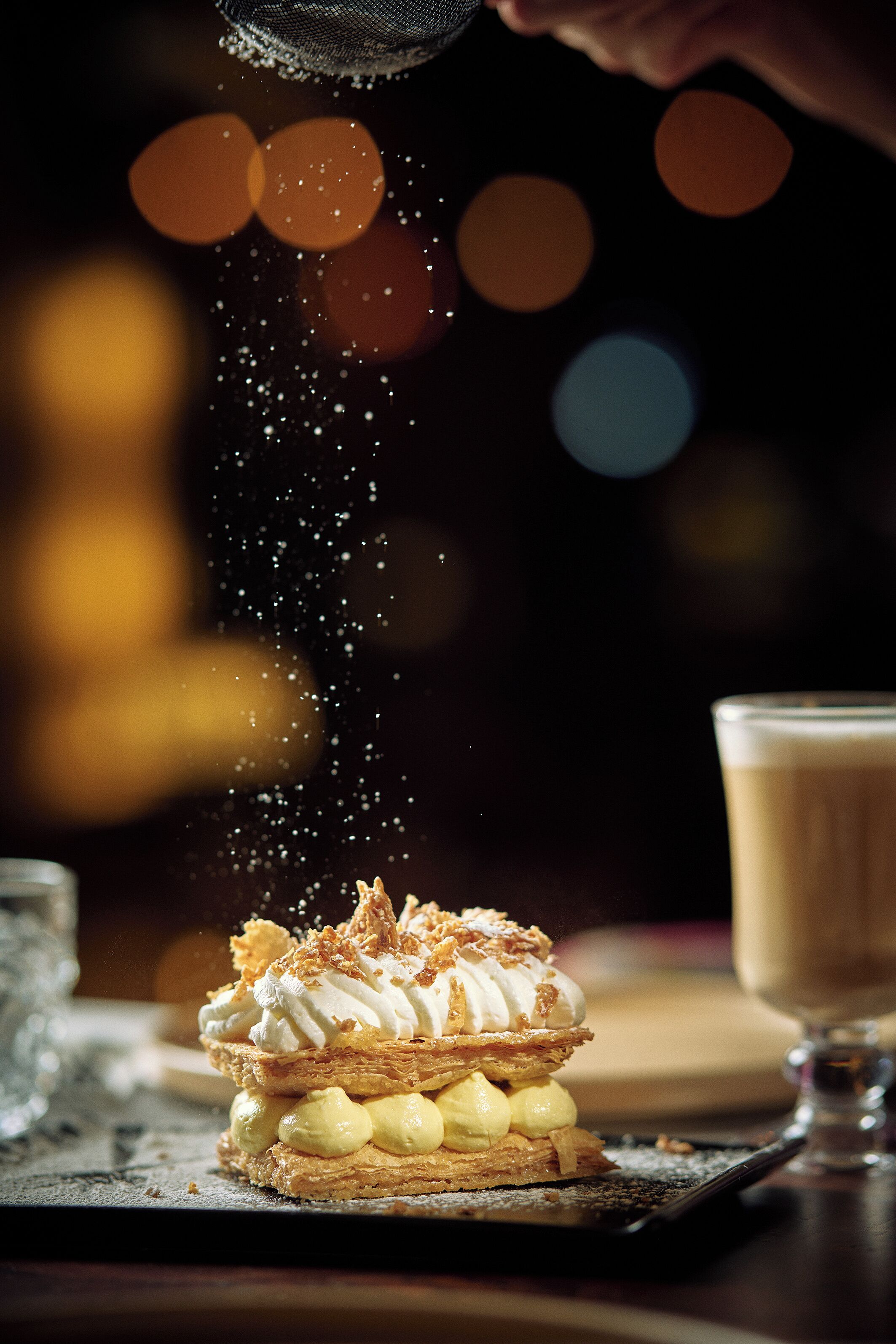A dessert with whipped cream and nuts, dusted with powdered sugar, on a plate.