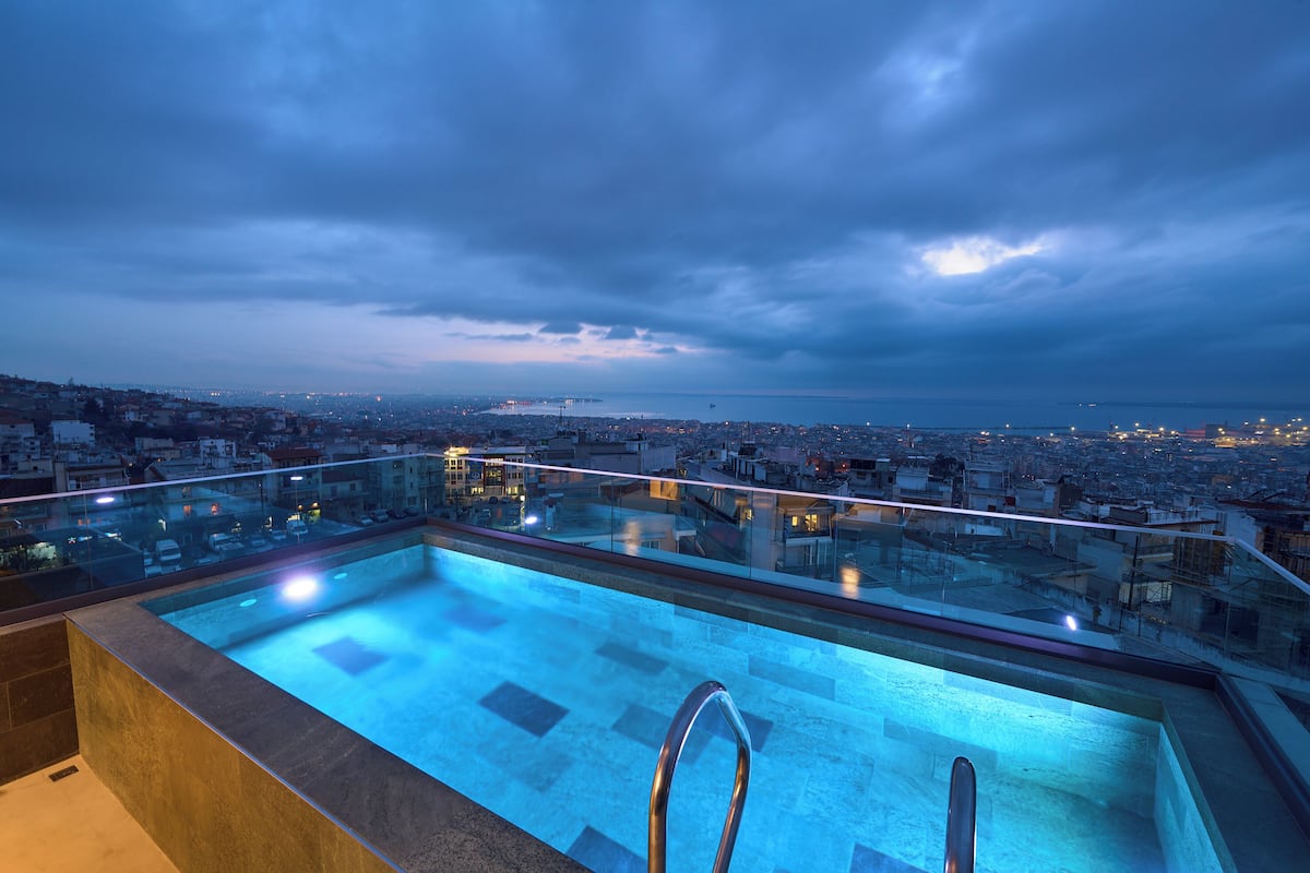 A rooftop pool with a glass balustrade overlooking a cityscape at dusk.