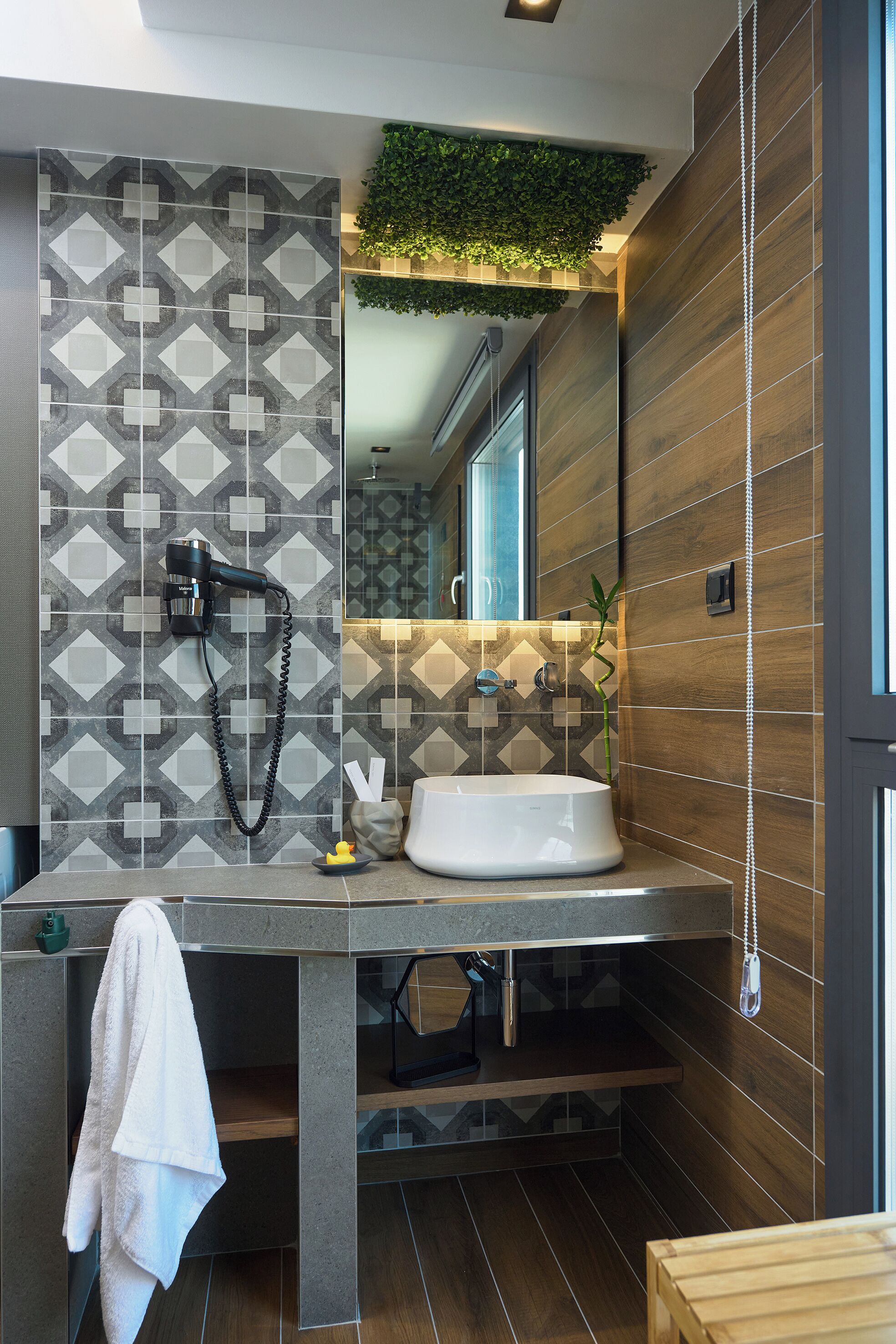 Un baño moderno con un salpicadero de azulejos geométricos, un lavabo blanco y un jardín vertical integrado.