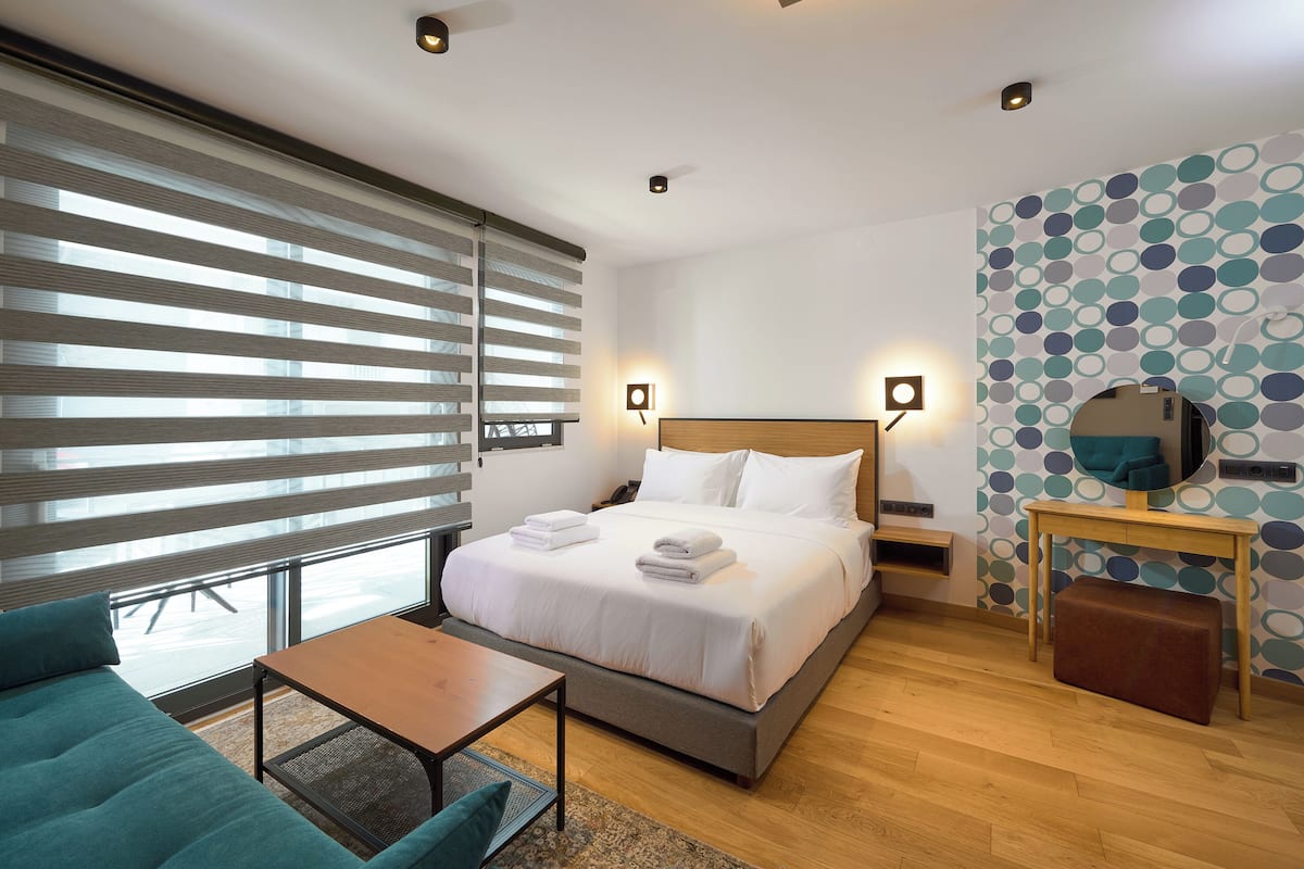 A modern hotel room with a large bed, a small table, a sofa, and a desk.