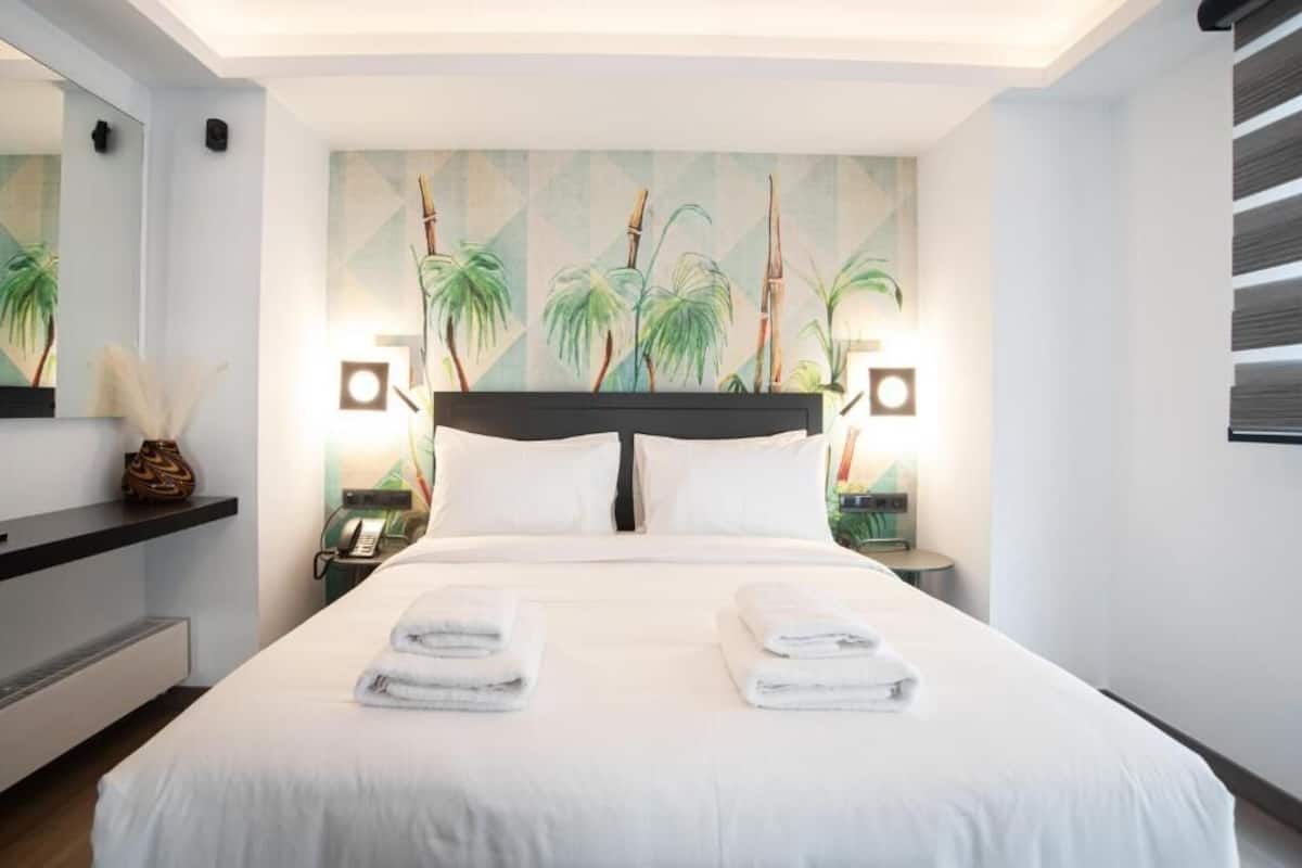 A modern hotel room with a large bed, two bedside tables, a nightstand, a wall-mounted telephone, and a large mirror.