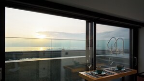 A balcony with a table set for two, overlooking a body of water and a distant cityscape during sunset. - SIGMA Suites Hotel (Neapoli-Sykies)