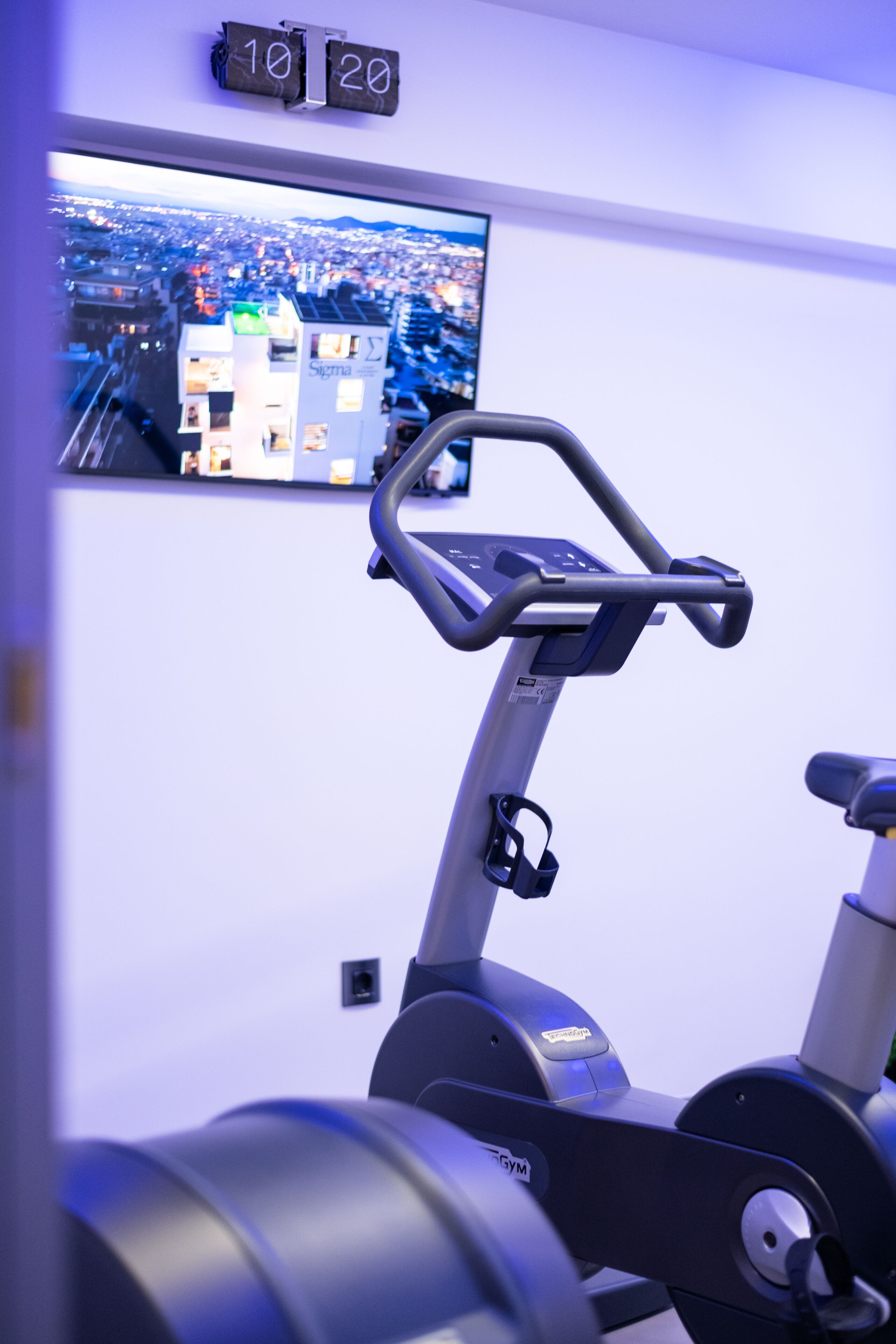 Una máquina de ejercicio con pantalla digital y un televisor montado en la pared mostrando un paisaje urbano.