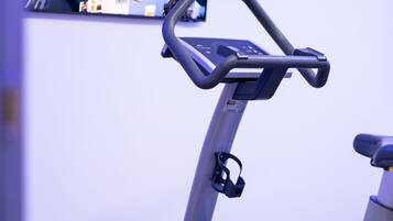 Una máquina de ejercicio con pantalla digital y un televisor montado en la pared mostrando un paisaje urbano.